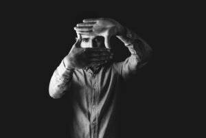 Black and white portrait of a man framing his face with his hands, creating an artistic, moody effect.